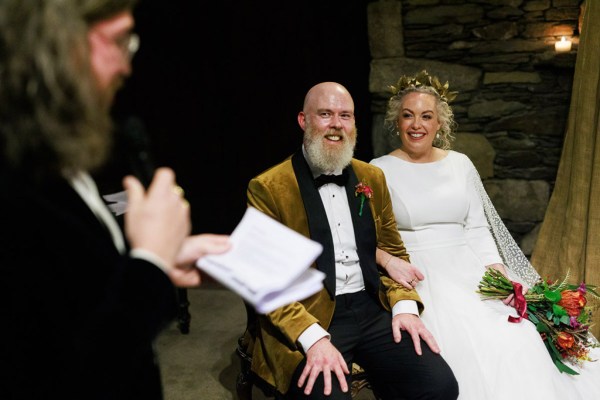 bride and groom sit at the alter on chairs as celebrant reads sermon