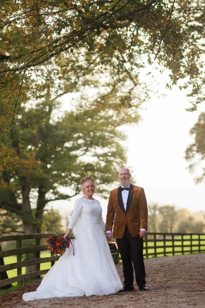 bride and groom stand in front of gate to forest garden setting trees surround