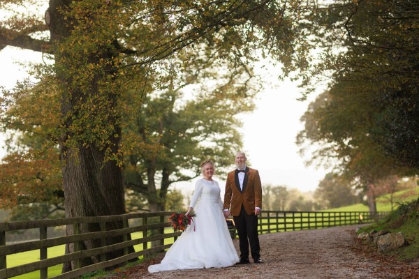 bride and groom stand in front of gate to forest garden setting trees surround