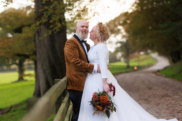 bride and groom against gate to forest setting she looks at him