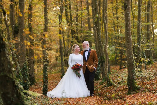 bride and groom stand inside forest surrounded by trees autumnal vibe