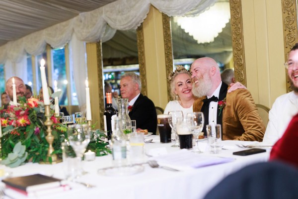 bride groom and father sit at the dining room table together he kisses her on the cheek