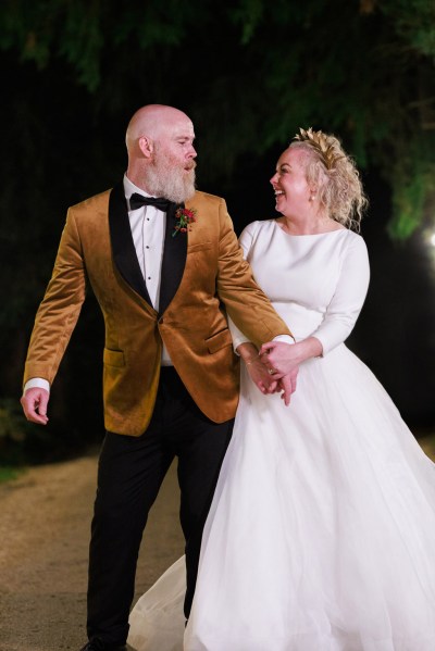 nighttime shot of bride and groom holding hands on the pathway laughing smiling