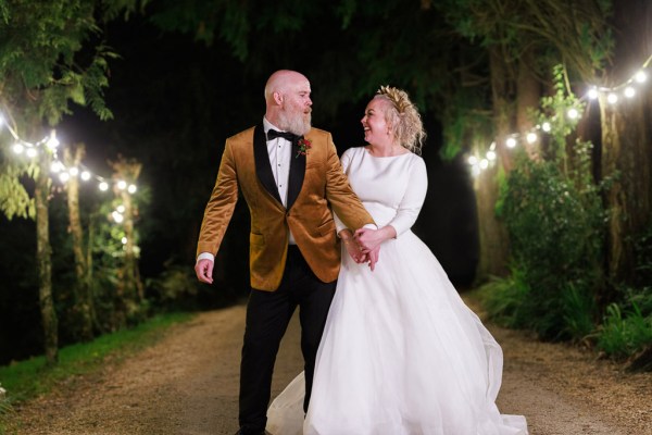 nighttime shot of bride and groom holding hands on the pathway laughing smiling