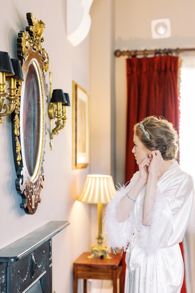 bride puts on her earrings in mirror