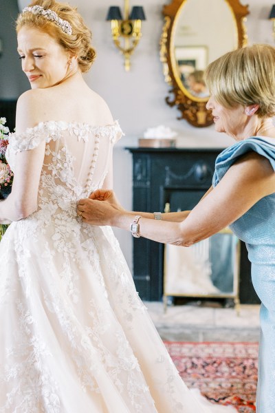 mother in blue dress helps bride with bridal gown