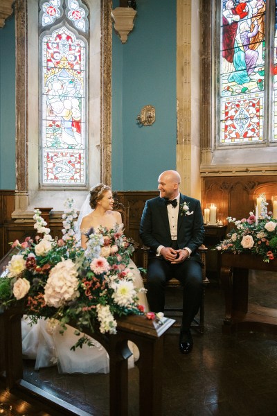 bride and groom sit at the alter flowers on table chapel church setting