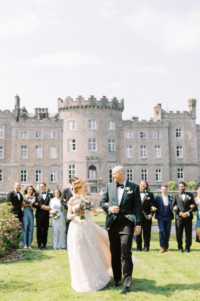 bride and groom standing on grass in front of wedding venue castle and guests