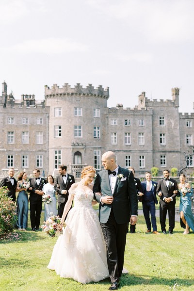 bride and groom standing on grass in front of wedding venue castle and guests