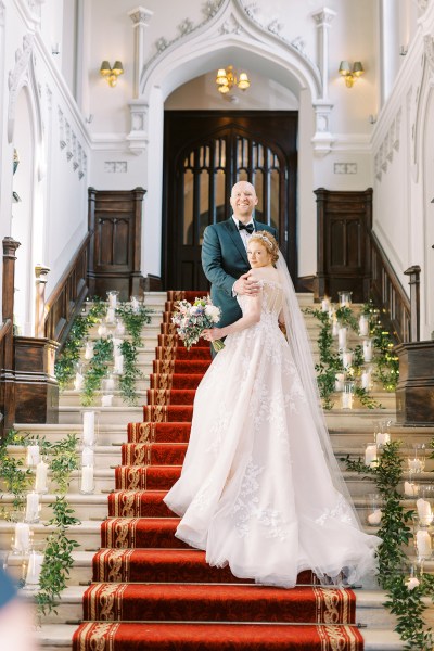 bride and groom walks up staircase lights candles on stairs red carpet