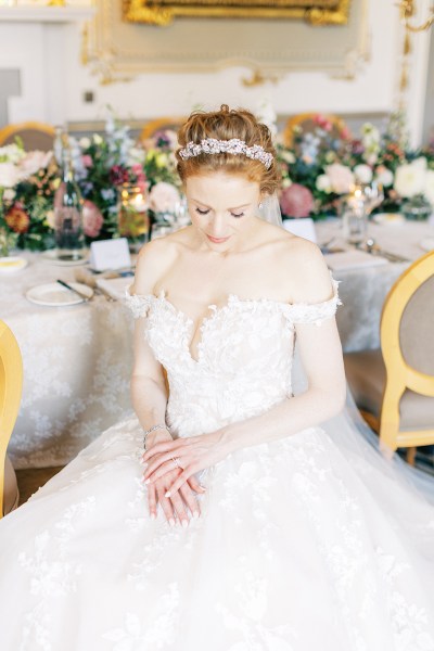 bride looks down hand over hand on lap shows off hair accessory