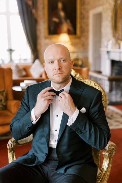 groom wearing tuxedo fixing up bowtie