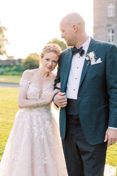 bride and groom hold arms on grass setting outside wedding venue