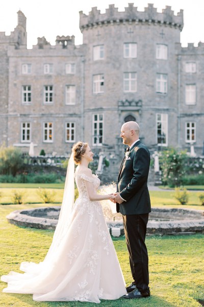 bride and groom hold hands in front of fountain and wedding venue