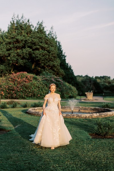 bride standing in garden trees fountain sun setting