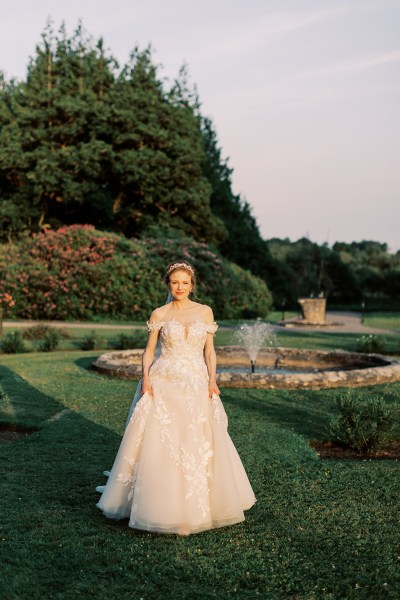 bride standing in garden trees fountain sun setting