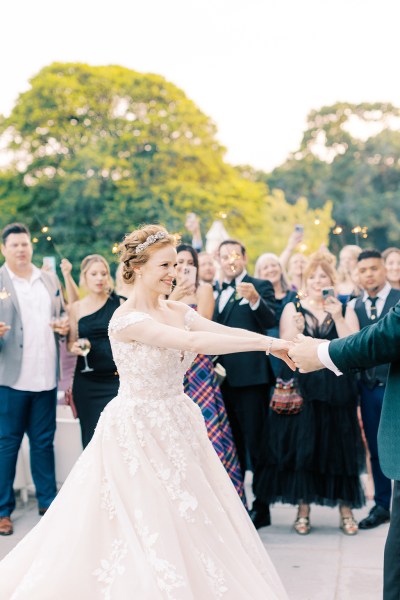 bride and groom hold hands and dance as guests clap