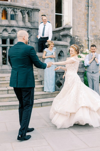 bride and groom hold hands and dance as guests clap