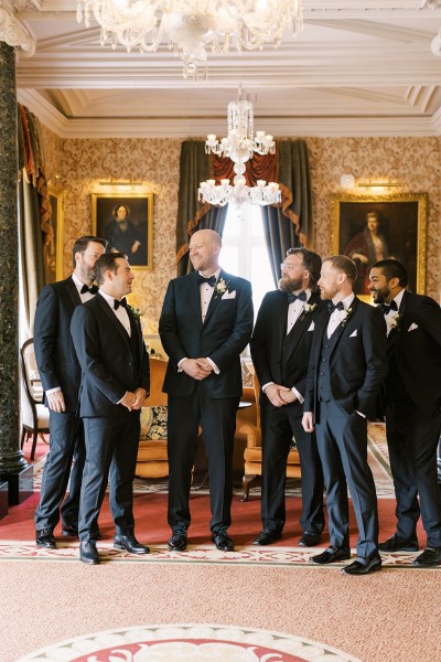 groom and groomsmen stand on red carpet waiting