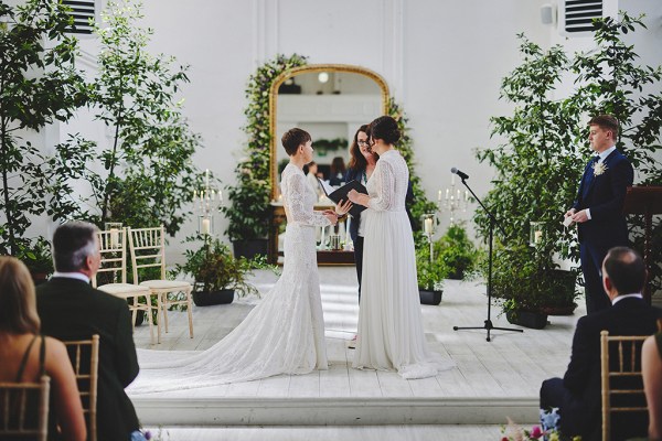 Brides stand in front of guests during wedding ceremony