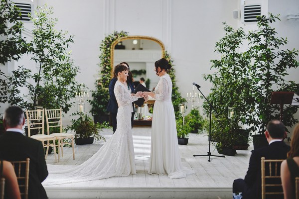 Brides stand in front of guests during wedding ceremony with yellow ribbon