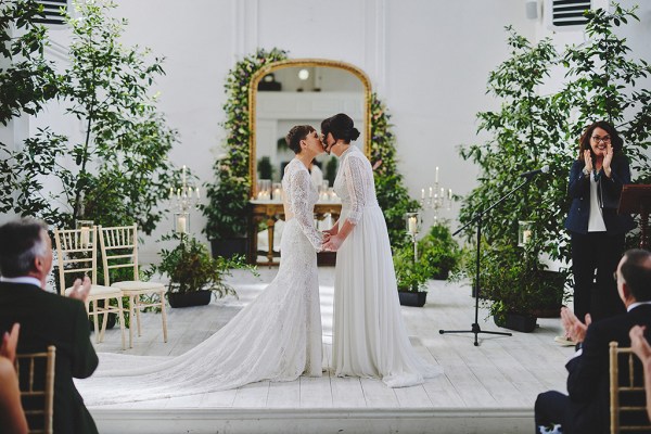 Brides stand in front of guests during wedding ceremony with yellow ribbon they kiss