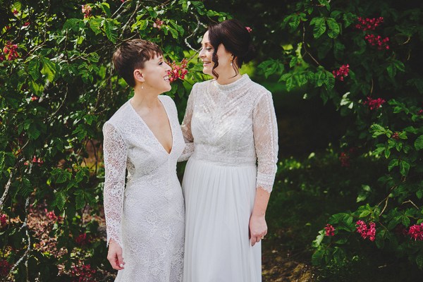 Brides look at each other in garden setting hedge bush