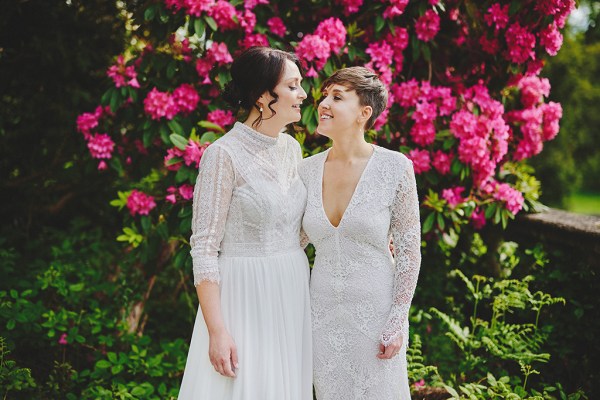 Brides stand smiling in front of pink roses flowers