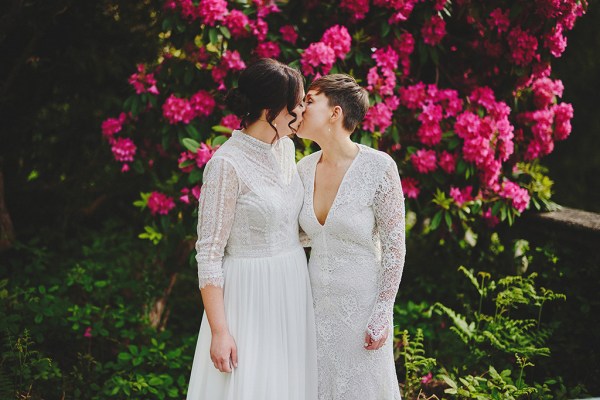 Brides stand smiling in front of pink roses flowers kissing