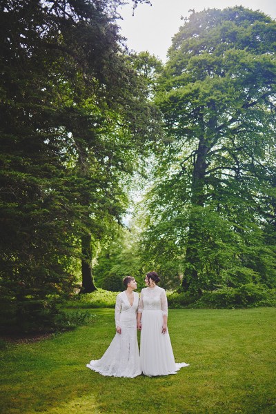 Brides stand on grass in forest garden setting