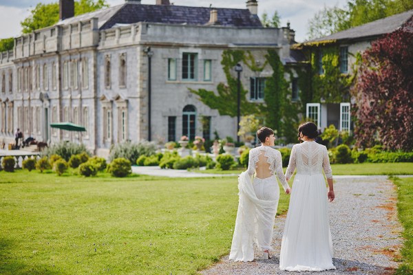 Brides walk hand in hand towards wedding venue from behind