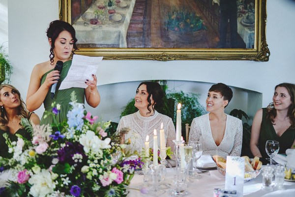 Brides sit at dining room ballroom table watching speeches take place