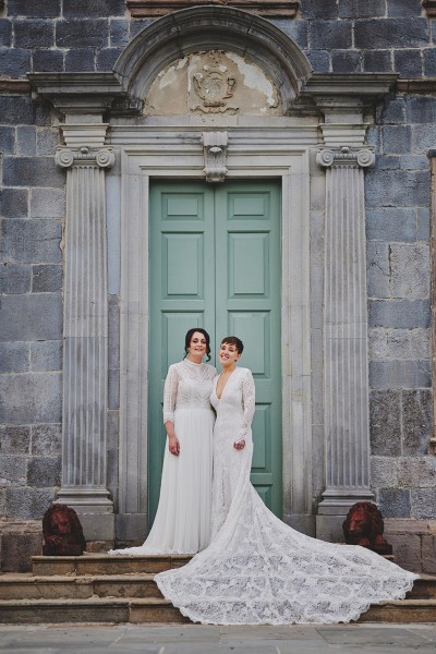 Brides stand at blue door entrance to wedding venue