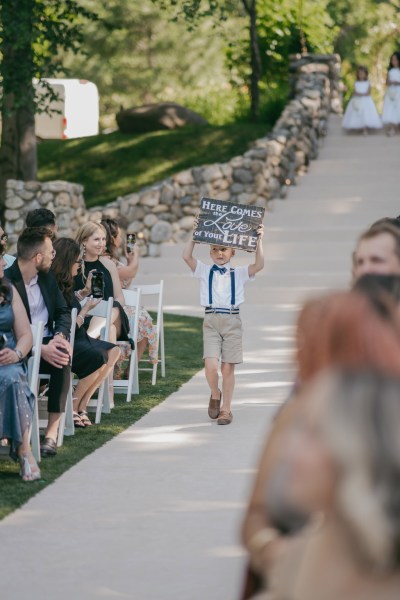 here comes love of your life sign boy holding it up written in chalk walking down aisle