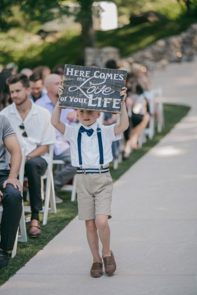 here comes love of your life sign boy holding it up written in chalk walking down aisle