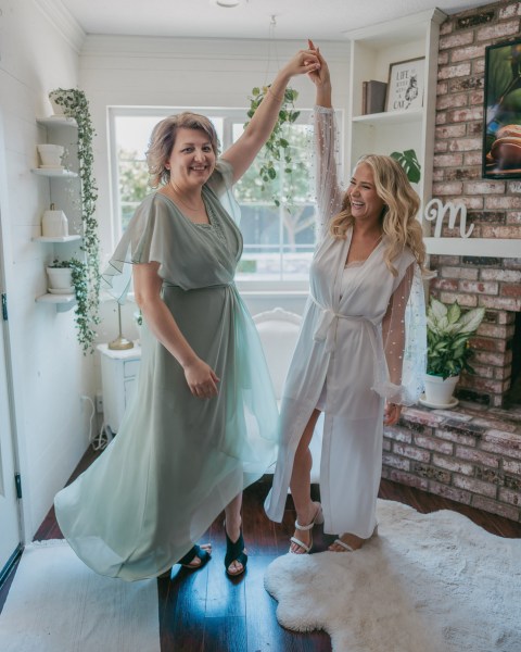 bride and her mother get ready together hands/arms in the air