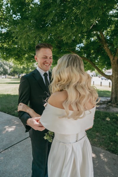 bride and groom stand on pathway to garden smiling they embrace