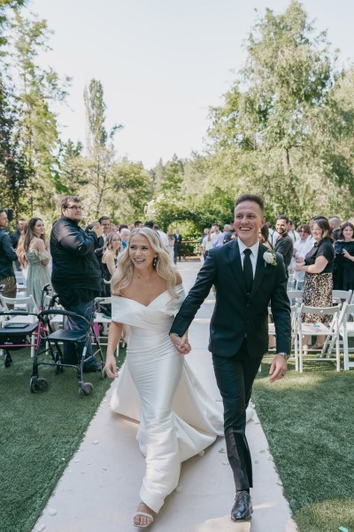 bride and groom exit wedding ceremony all smiles while guests clap in background