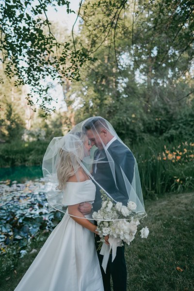 bride and groom laughing as they touch foreheads covered in her veil