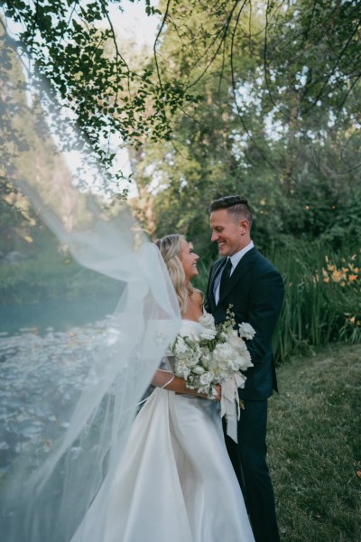 bride and groom look at each other in the garden while the veil is blowing in the wind