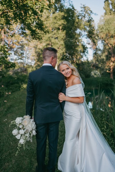 Bride rests her head on grooms shoulder as he holds her white bouquet flowers