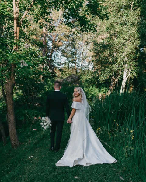 bride and groom walk away in garden she looks over shoulder