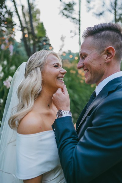 bride and groom face each other and laugh he puts his hand on her chin