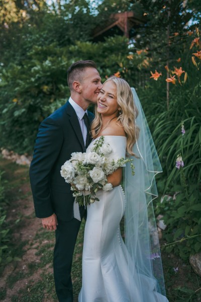 groom kisses the bride on the cheek in forest setting