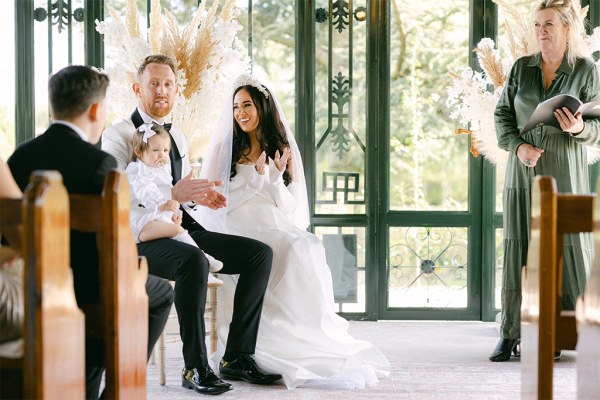 Little girl sits on grooms lap with bride smiling