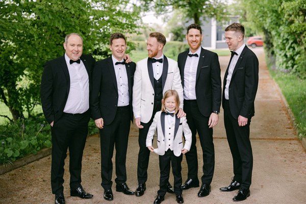 Groom his son in matching bowtie suit and groomsmen pose in forest setting