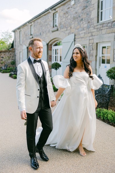 Bride and groom walk hand in hand down the pathway to wedding venue