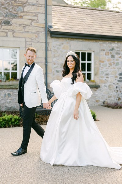 Bride and groom walk hand in hand down the pathway to wedding venue