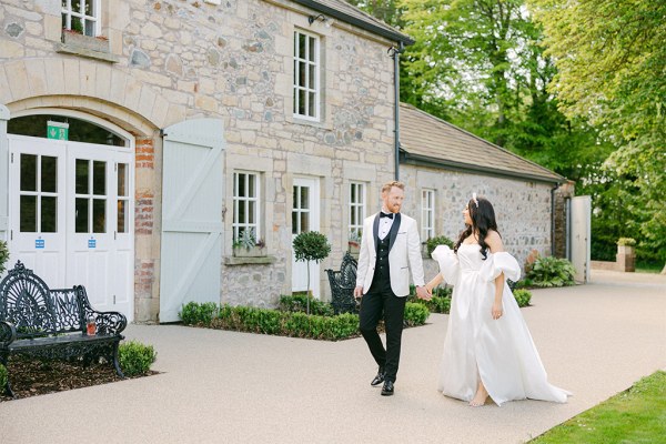 Bride and groom walk hand in hand down the pathway to wedding venue