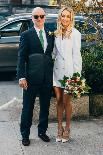 bride and groom stand together smiling he wears sunglasses she holds bouquet